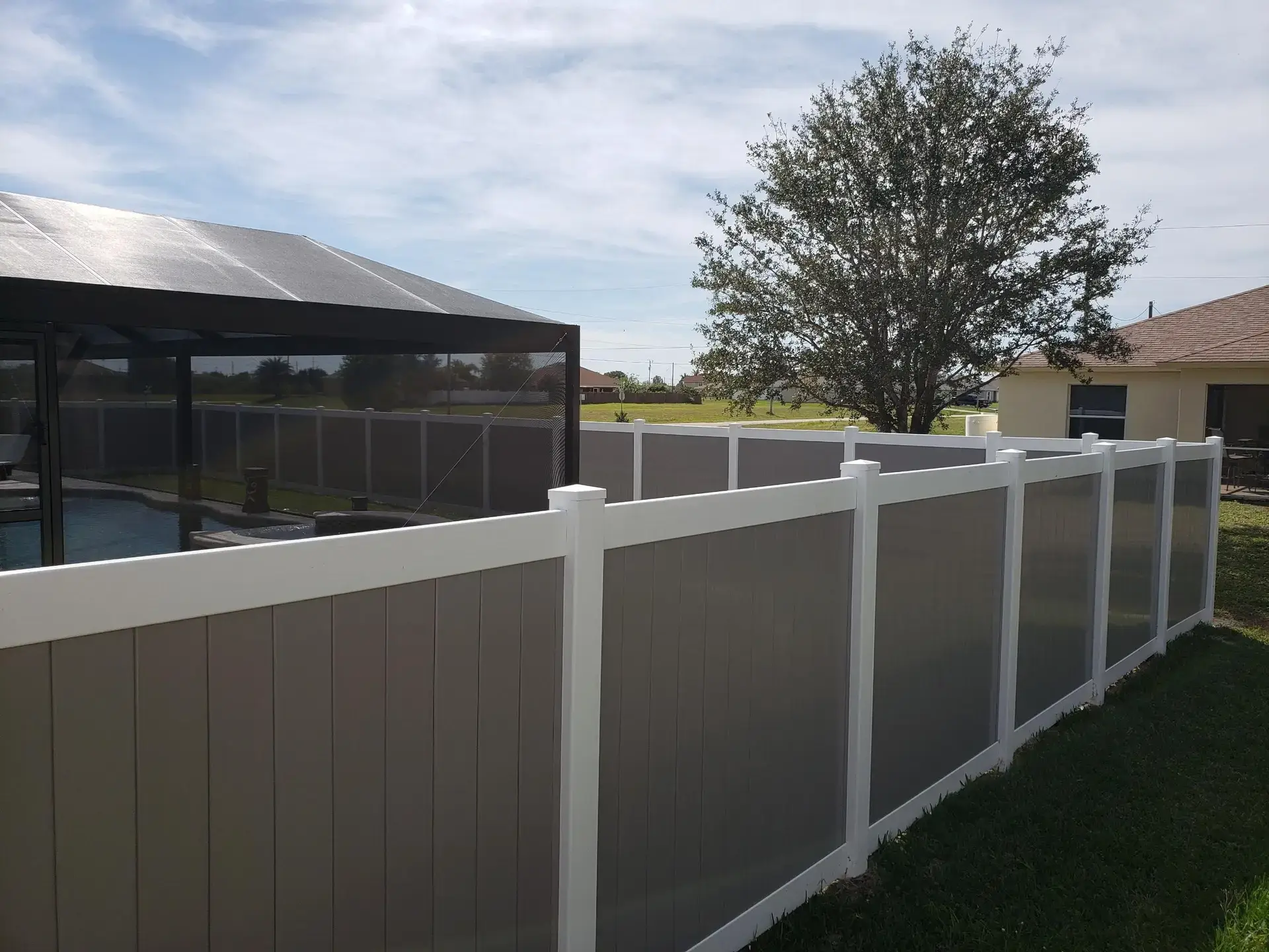 Two-tone grey and white vinyl privacy fence beside a screened pool cage by Premier Fence of SWFL